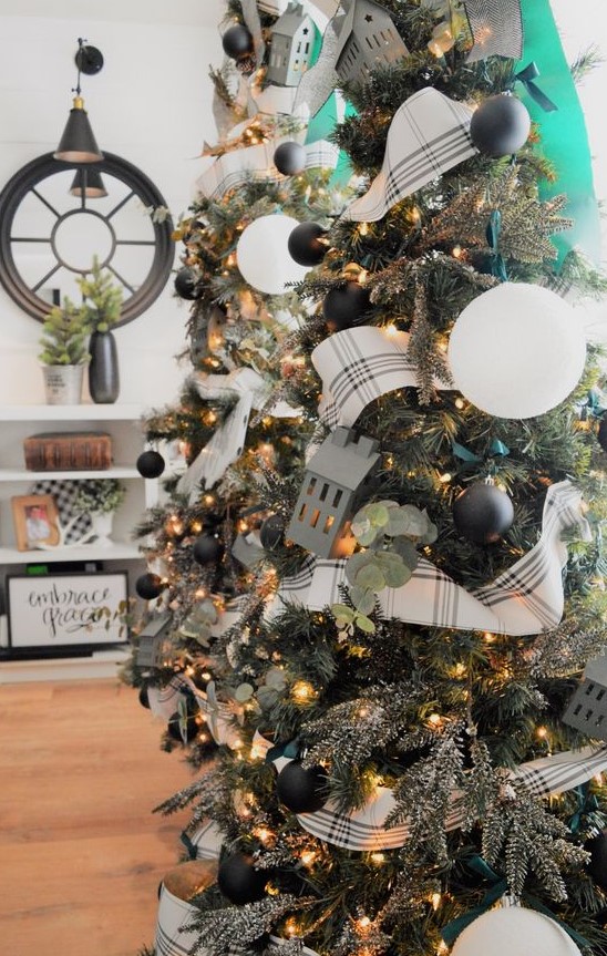 a Christmas tree decorated with small black and large white ornaments, lights, greenery and plaid ribbons is a chic idea