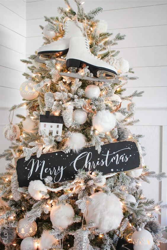 a black and white Christmas tree with lights, fluffy pompoms and white ornaments, skates and a chalkboard sign