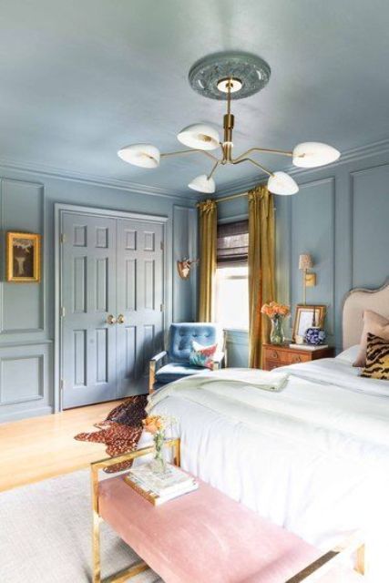 a blue eclectic bedroom with a neutral bed and bedding, a pink bench, a blue chair, gold drapes and a chandelier