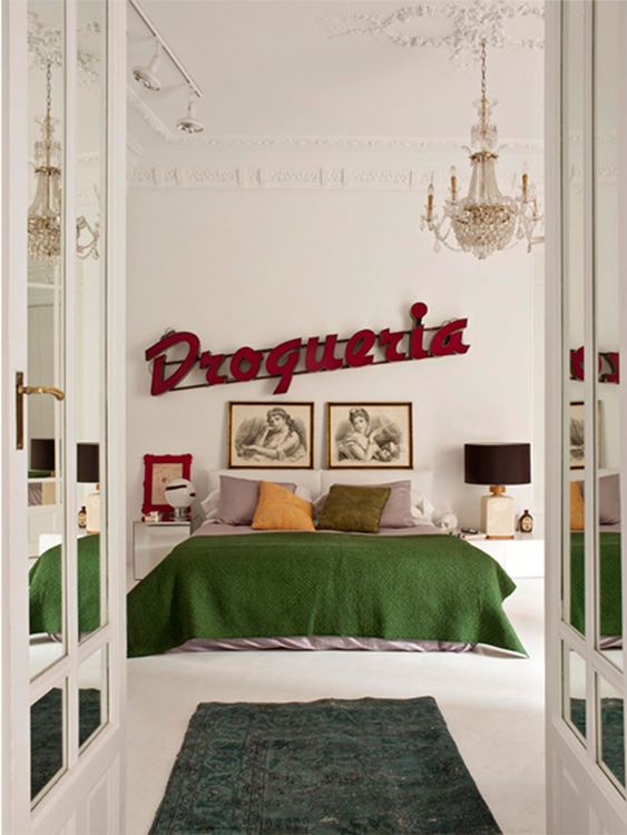 a fantastic eclectic bedroom with a bed and muted bedding, mismatching nightstands, lamps, a marquee light and a vintage chandelier