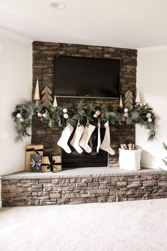 a fireplace mantel with evergreens, black and white ornaments, white stockings and faux trees on the mantel