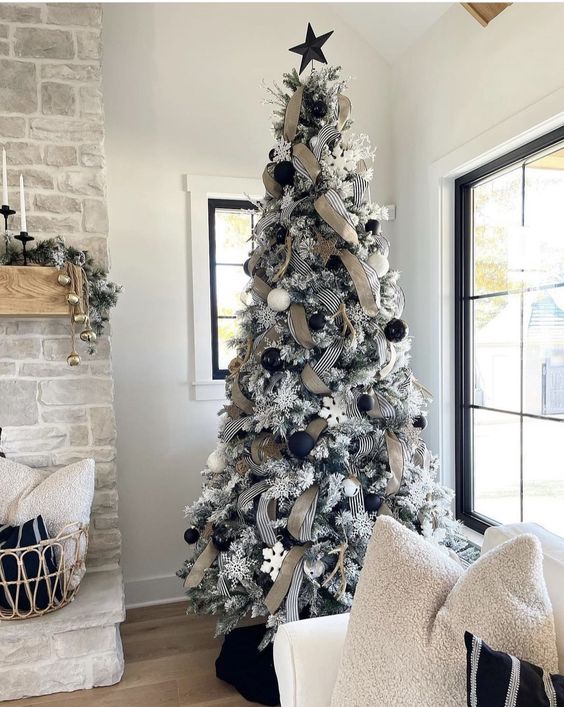 a flocked Christmas tree with black and white ornaments, striped and burlap ribbon, white snowflakes and a black star topper