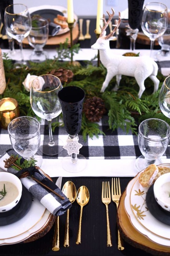 a lovely Christmas tablescape with a buffalo check runner and napkins, evergreens, pinecones, deer, candles and touches of gold for more chic