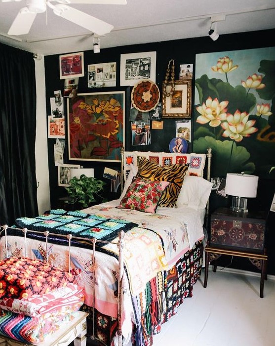 a maximalist guest bedroom with black walls, a metal bed, a refined inlaid nightstand, a bold gallery wall and colorful textiles