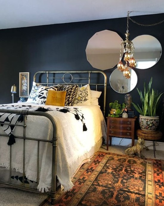 a moody eclectic bedroom with boho rugs and a chandelier, vintage mirrors and a metal bed and mid century modern nightstands