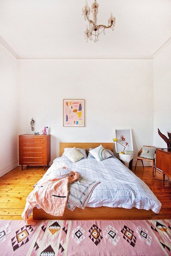 a pretty eclectic bedroom with mid-century modern stained furniture, bright textiles and artwork plus a vintage chandelier