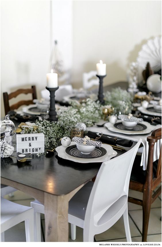 a vintage-inspired Christmas tablescape with black and white plates, black candleholders with candles, white blooms and pinecones