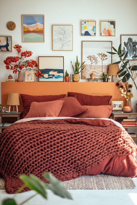 a warm-colored eclectic bedroom with a bed and terracotta bedding, an orange headboard, mismatching nightstands and a gallery wall