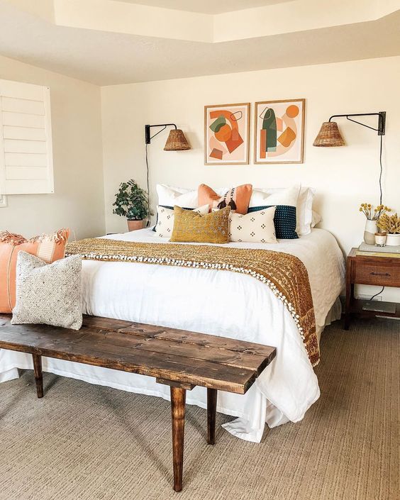 an eclectic bedroom with a bed and printed bedding, a stained bench, dark-stained nightstands, artwork and woven lamps