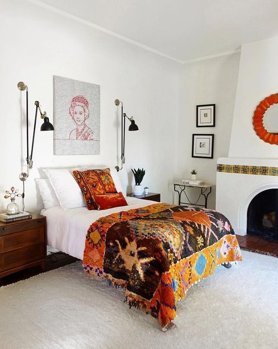 an eclectic bedroom with a vintage hearth with tiles, a bed with colorful bedding, dark-stained nightstands, black sconces and potted plants