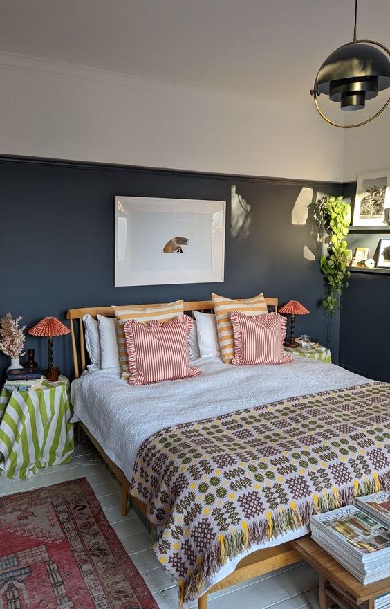 an eclectic bedroom with black walls, a bed with bright bedding, matching nightstands and lamps and a cool pendant lamp