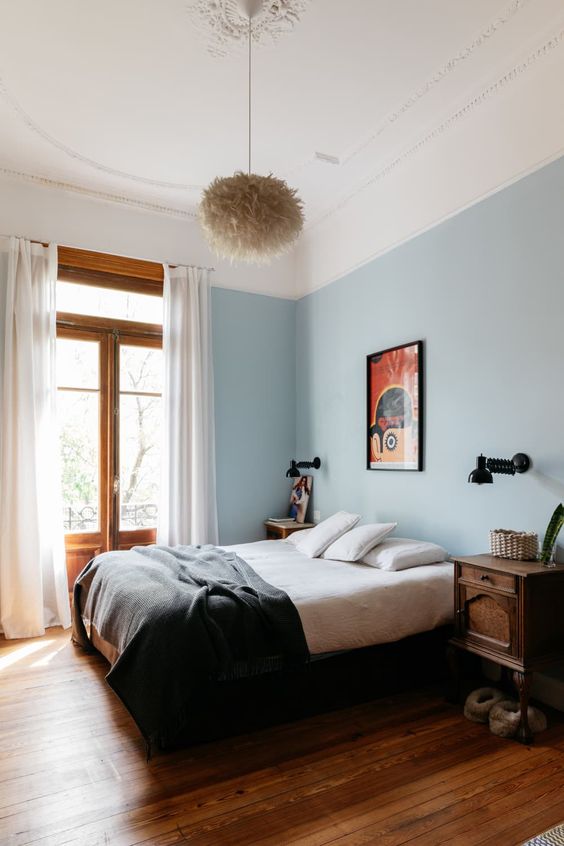 an eclectic bedroom with blue walls, dark-stained nightstands, bold artwork, a fluffy pendant lamp