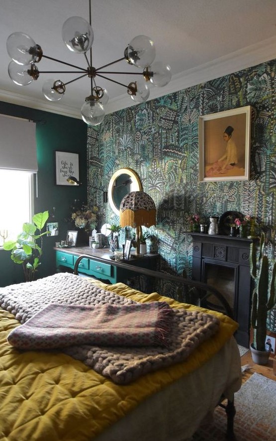 an eclectic bedroom with emerald walls and a botanical accent one, a black fireplace, an emerald vanity, a forged bed with bold bedding