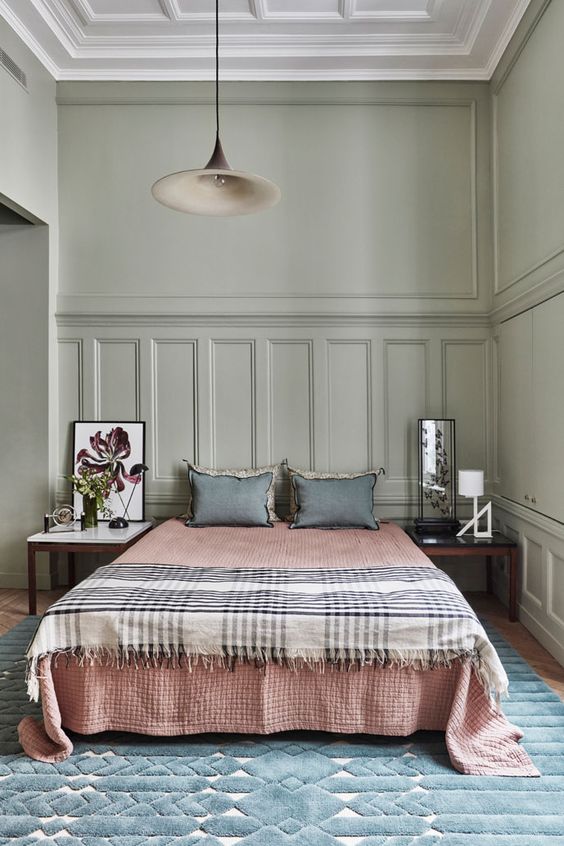 an olive green eclectic bedroom with paneling, a bed with muted color bedding, a pendant lamp and mismatching nightstands