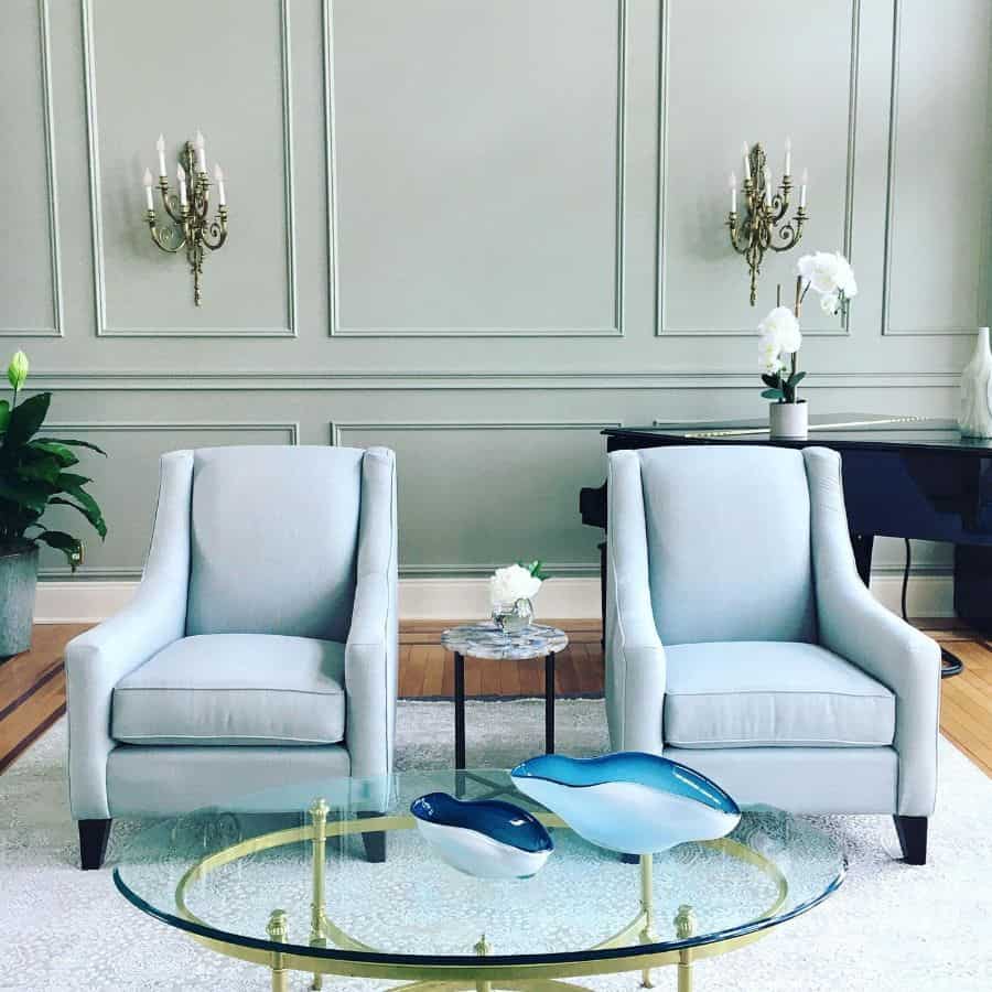 Green paneled wall, two blue accent chairs and a glass coffee table 