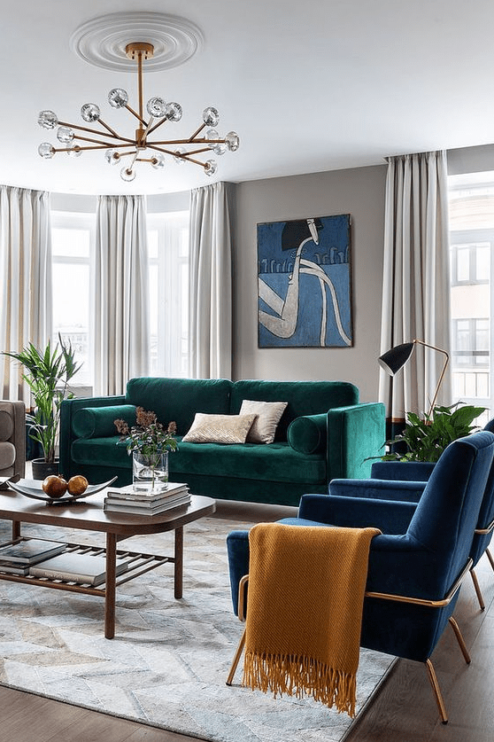a super bright living room with gray walls, a bold green sofa, navy blue chairs, a coffee table, a chandelier and some decor