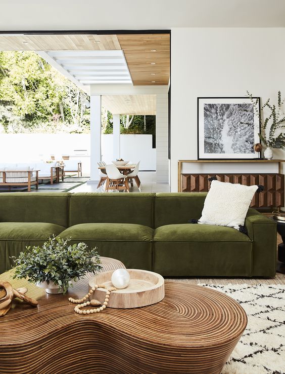 An elegant space with a low green velvet sofa, a unique curved coffee table, a console with decor and access to the terrace