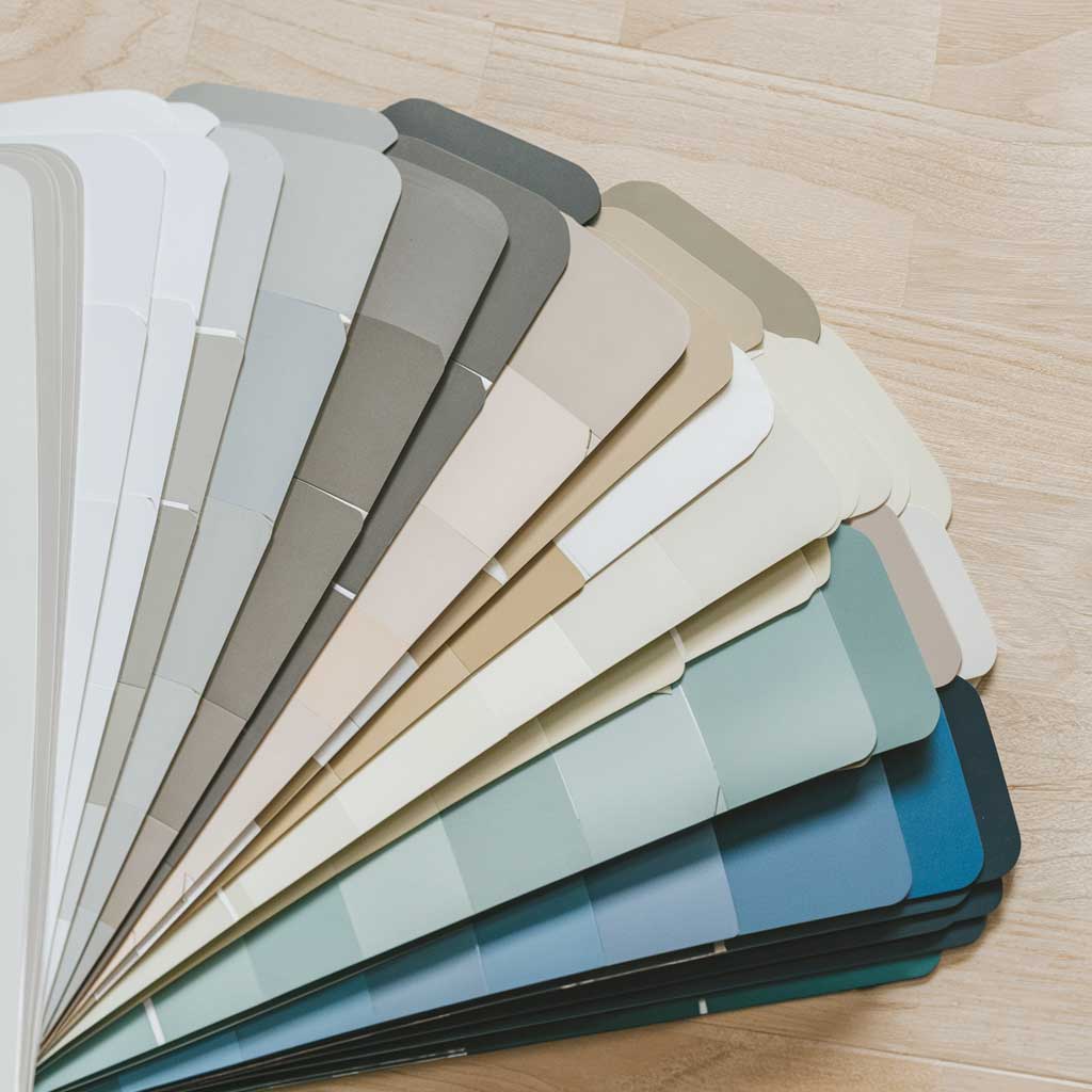 Color swatches ranging from crisp white to soft gray, beige, and muted blue on a light wooden surface, evoking Scandinavian flooring tones.