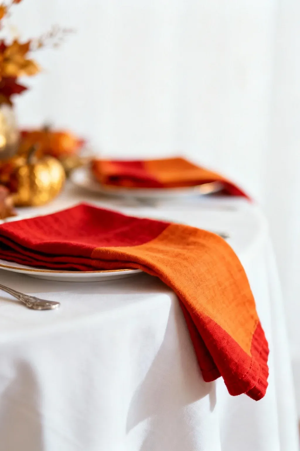 A white tablecloth with colorful cloth napkins in deep reds and oranges.
