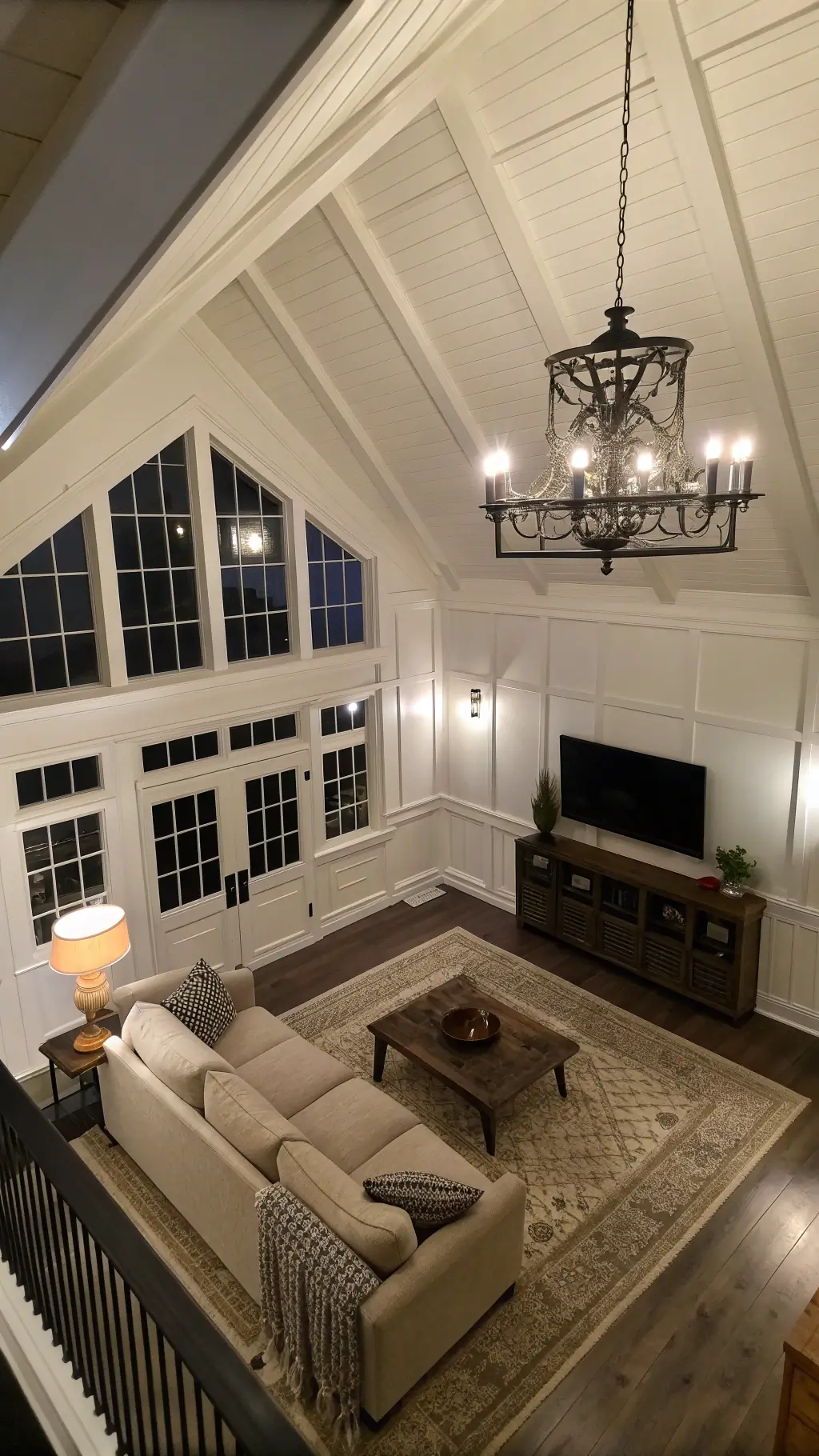 Cozy family room with creamy white board and batten walls, coffered ceiling, greige fabric sofa, vintage wool rug, black iron chandelier at twilight