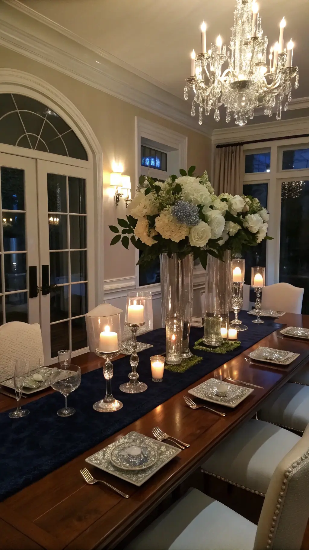 Elegant dining room with crystal hurricane vases filled with white hydrangeas and eucalyptus, mercury glass votives glowing