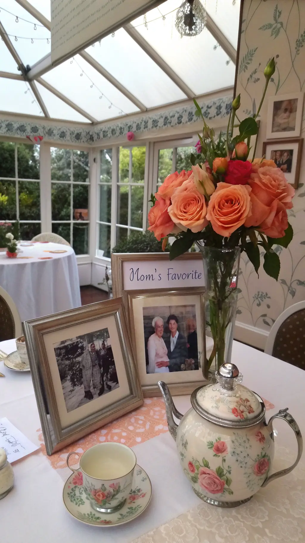 Sunlit conservatory dining area with family photos, garden roses in vintage teapot vase, and handwritten notes among flowers