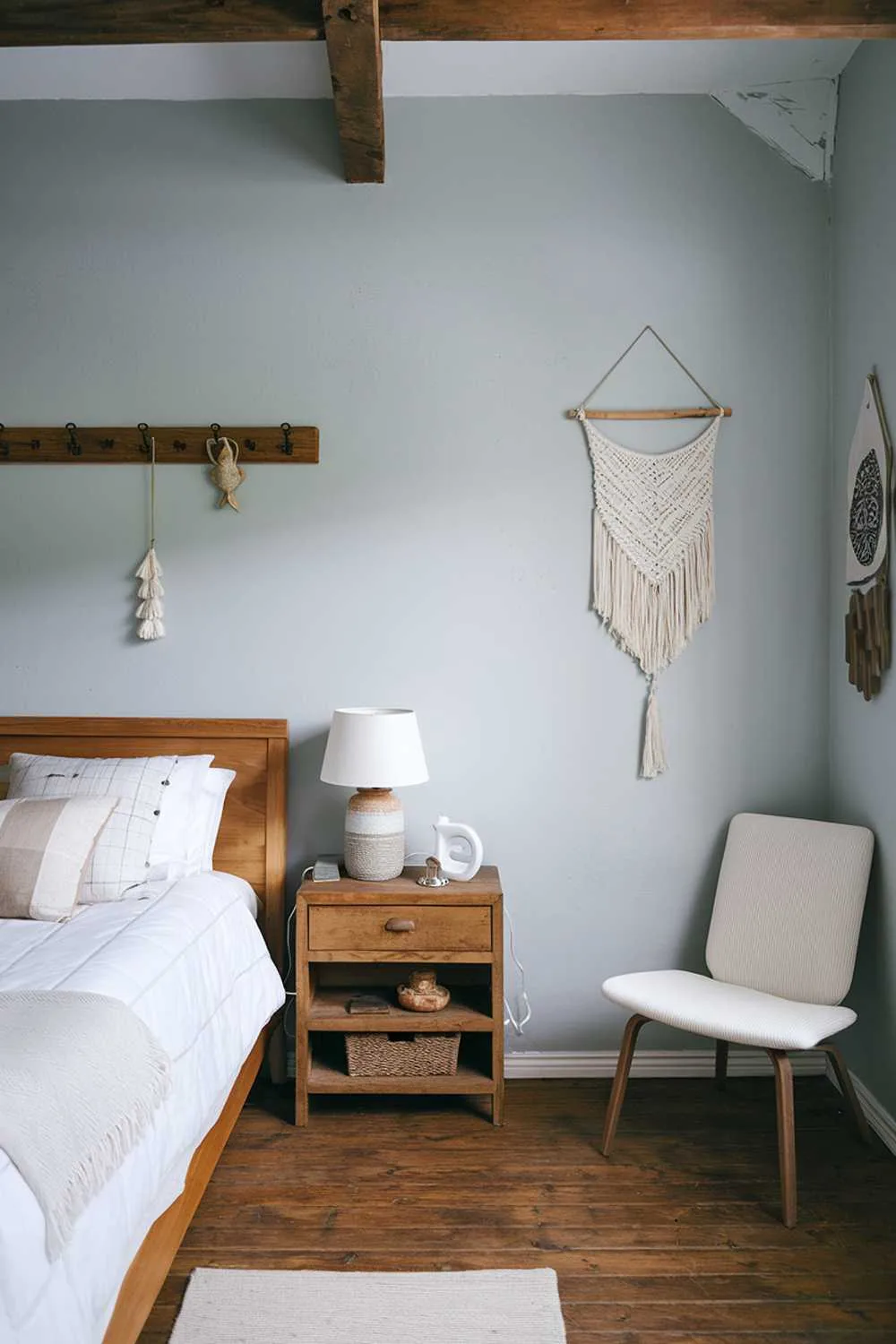 Scandinavian farmhouse bedroom with wooden bed, white blanket, light blue walls, and wooden beam ceiling.