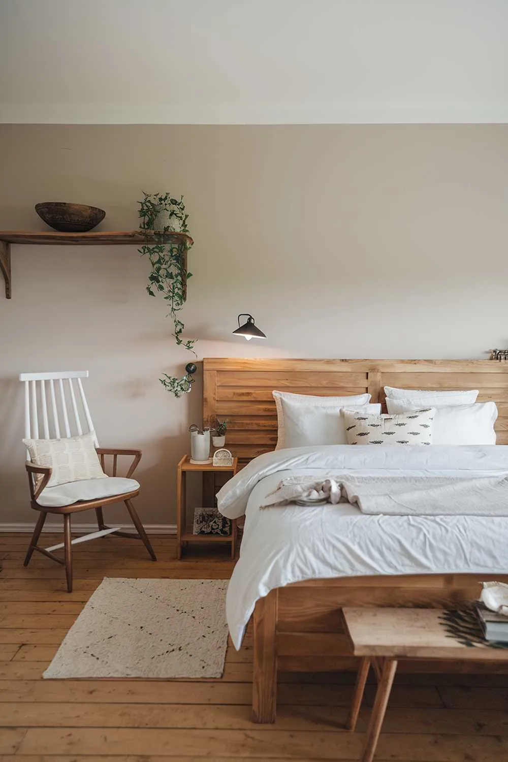 Scandinavian farmhouse bedroom with wooden bed frame, white duvet, wooden headboard, white chair, and soft beige walls.