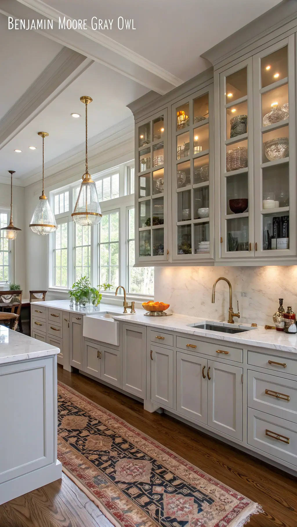 elegant farmhouse-style kitchen with ceilings ambient morning light benjamin moore owl painted pale gray cabinets glass-front uppers marble counters brass gooseneck faucet open shelving white ironstone collection lit by library lights and colorful vintage runner.