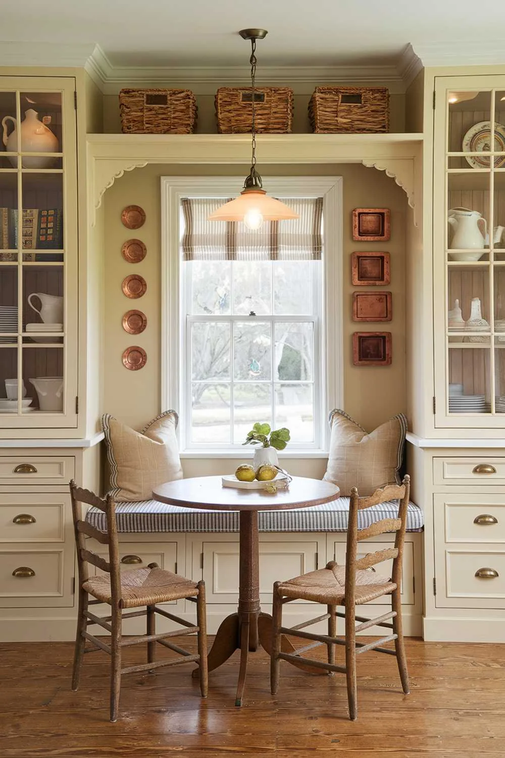 Multi-Functional Kitchen Spaces Cozy kitchen nook with a built-in window seat featuring storage drawers, flanked by tall cabinets, a small round table for dining, woven baskets on open shelves, and a vintage pendant light adding ambiance.