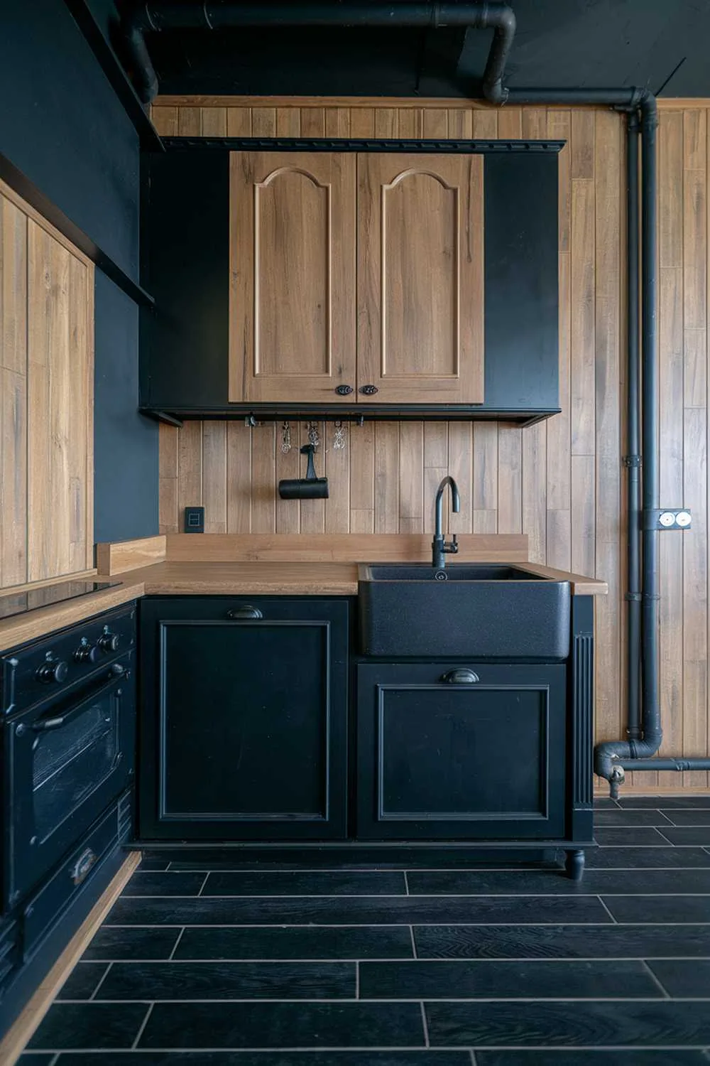 Kitchen with black countertop edged in wood, black sink, wood-paneled wall, and black pipe details