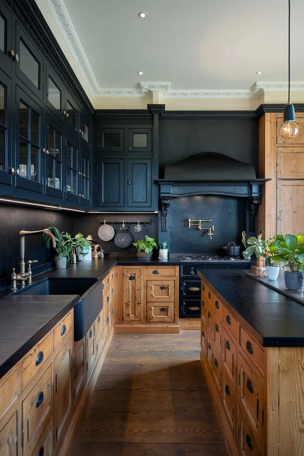 Kitchen with black countertops, wooden island, black and wood cabinets, black sink with wooden faucet, and potted plants