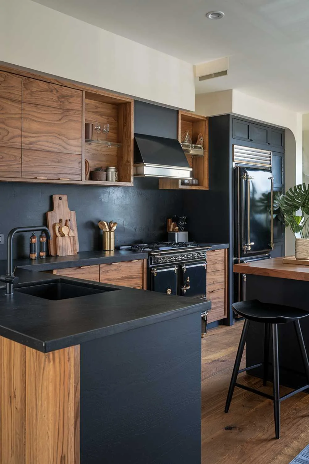 Kitchen with black countertops and backsplash, wood cabinets, black appliances with wood accents, black island with wood top, and potted plant