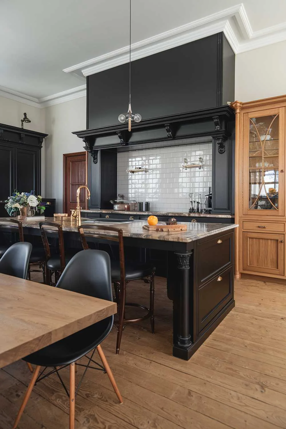 Spacious kitchen with black island featuring marble countertop, wood dining table, black chairs with wooden legs, and white tile backsplash