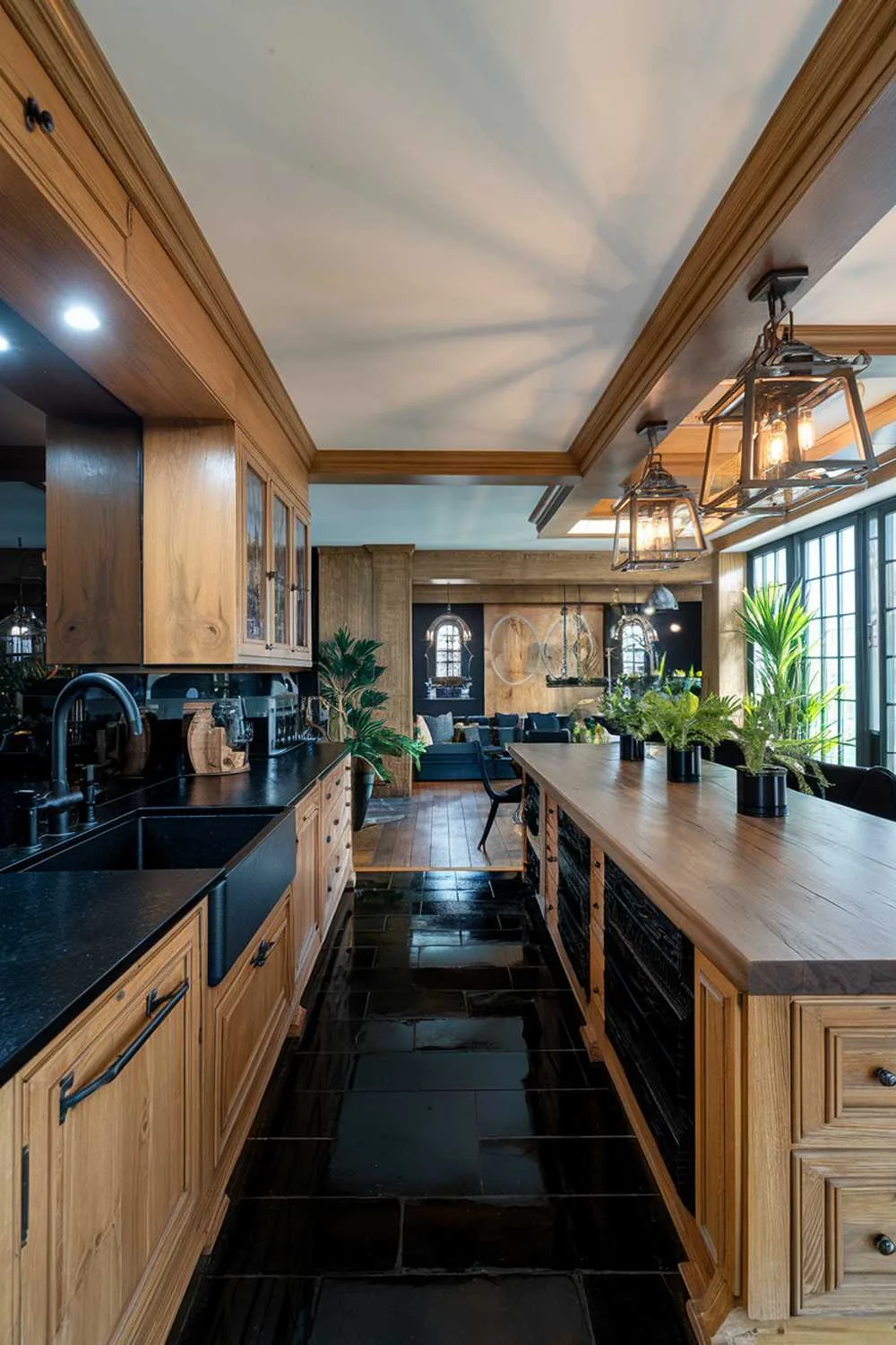 Kitchen with black countertop and backsplash, wooden cabinets and island, black sink and faucet, potted plants, and black tiled floor