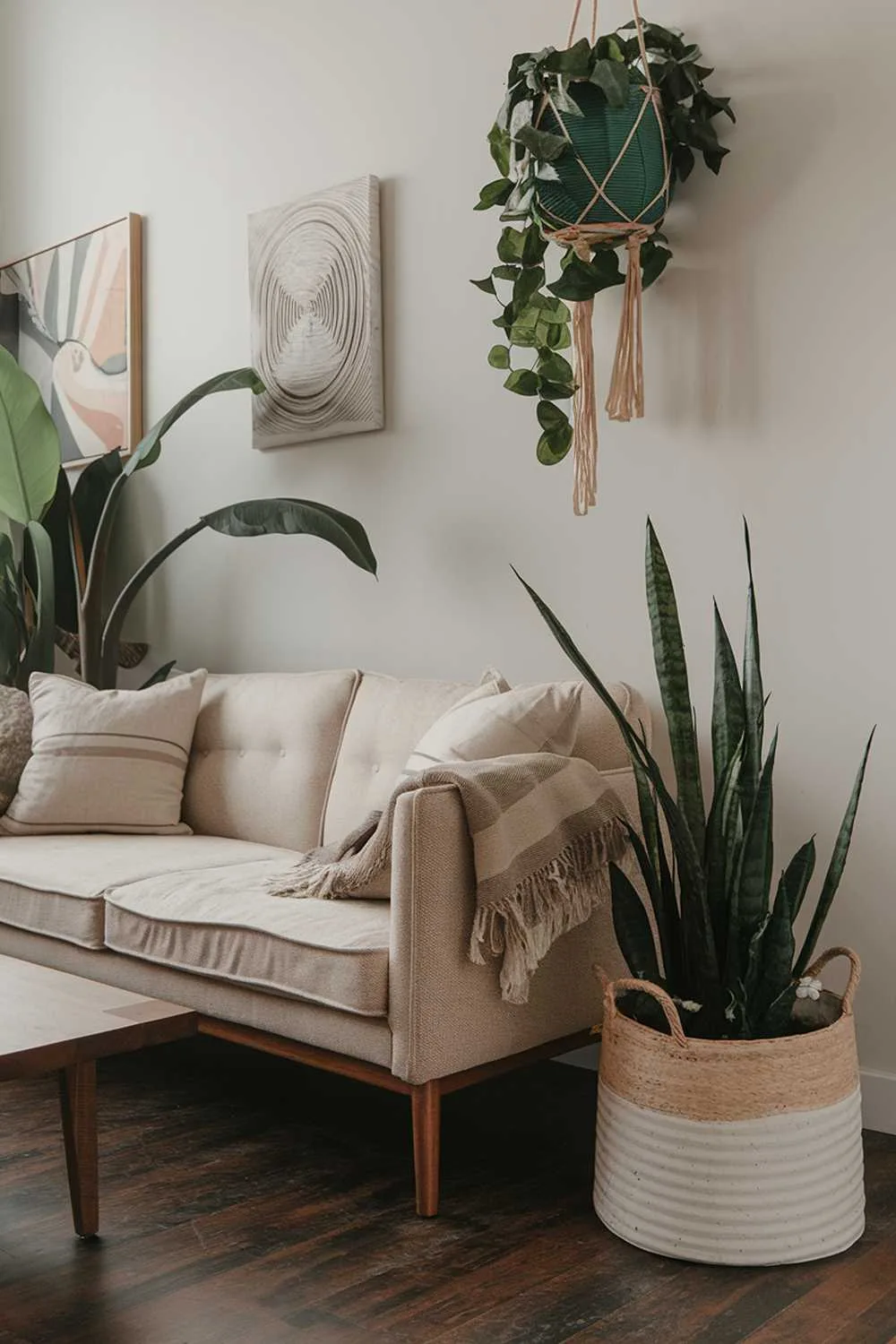 Close-up of beige sofa with throw pillows, wooden coffee table, large plant, hanging greenery, and dark wood floor.
