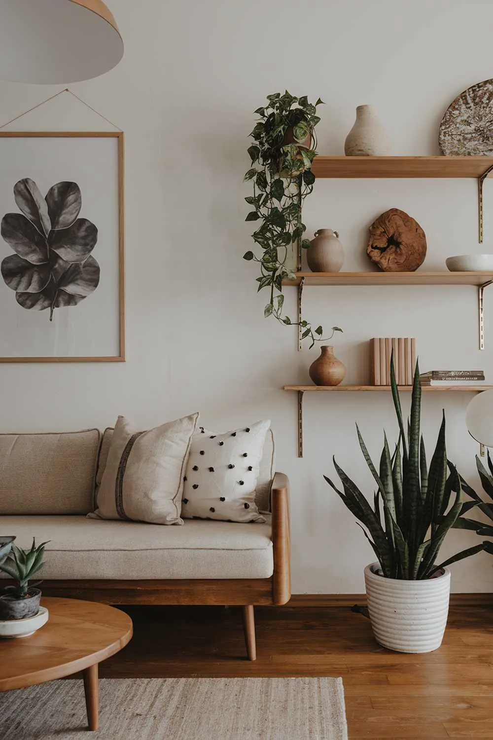Beige sofa with cushions, wooden coffee table, potted plants, wall art, shelves with decor, wooden floor, and soft lighting.