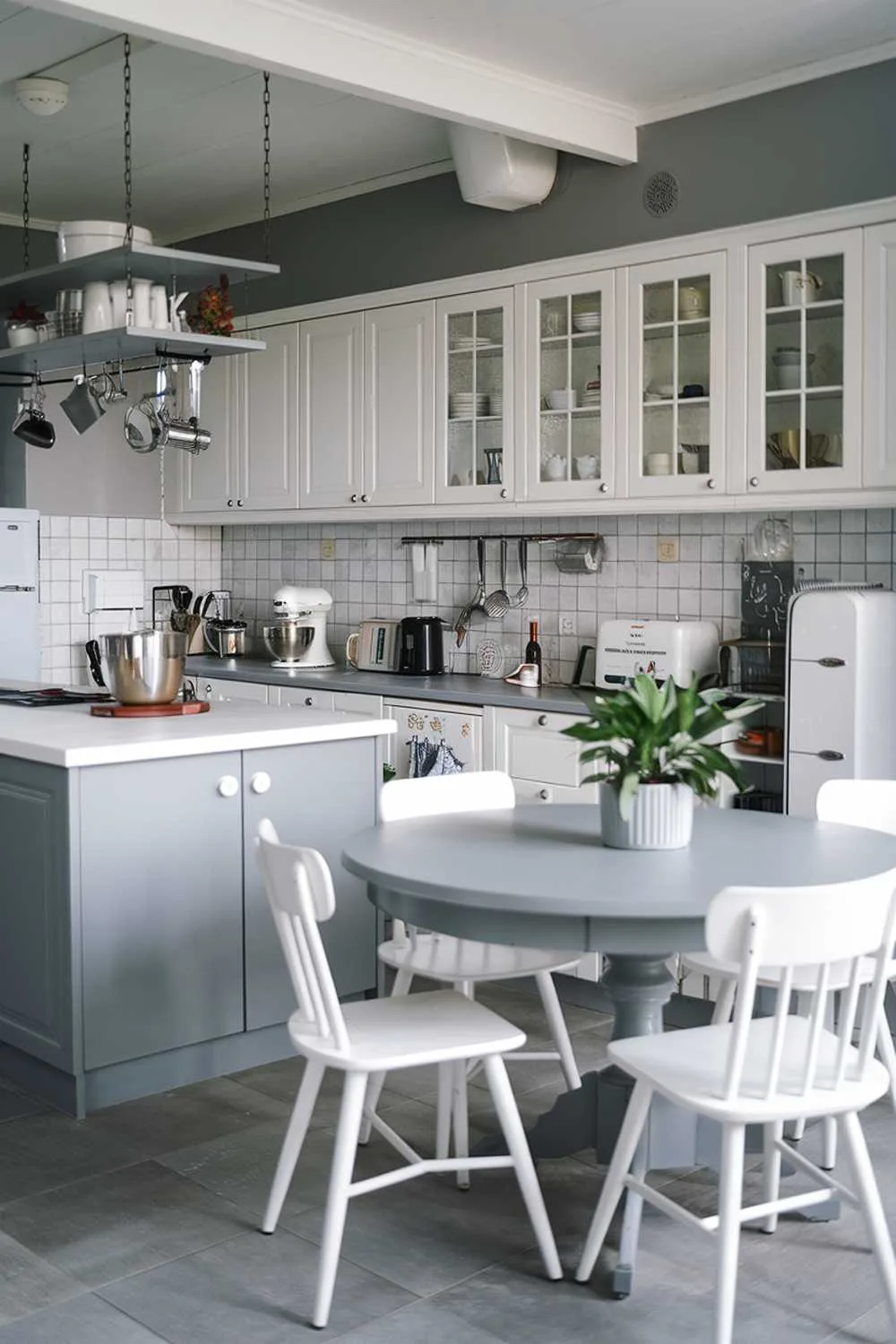 Gray kitchen island with white countertop, round gray dining table, white chairs, and gray backsplash.