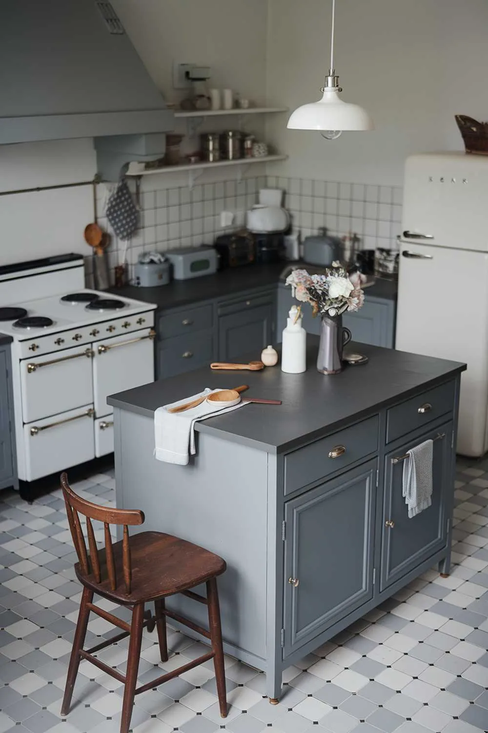 Gray kitchen island with dark countertop, vase of flowers, white stove, gray hood, and white refrigerator.