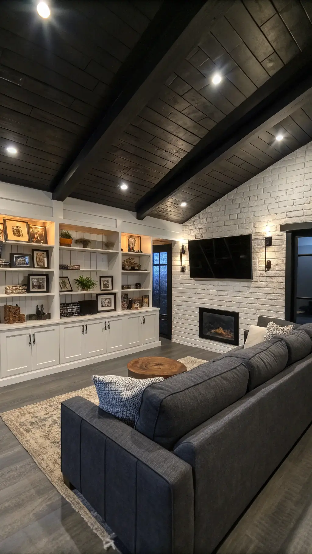 Contemporary farmhouse media room with black ceiling, white oak built-ins, industrial pipe shelving, and modern charcoal sectional during blue hour.